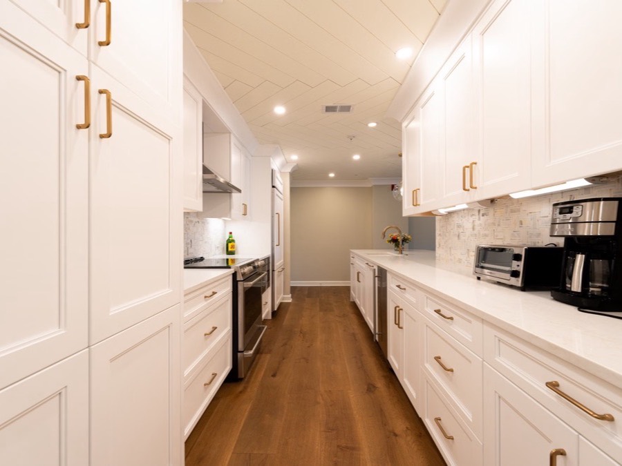 A finished white kitchen with brass cabinet pulls and a wood floor.